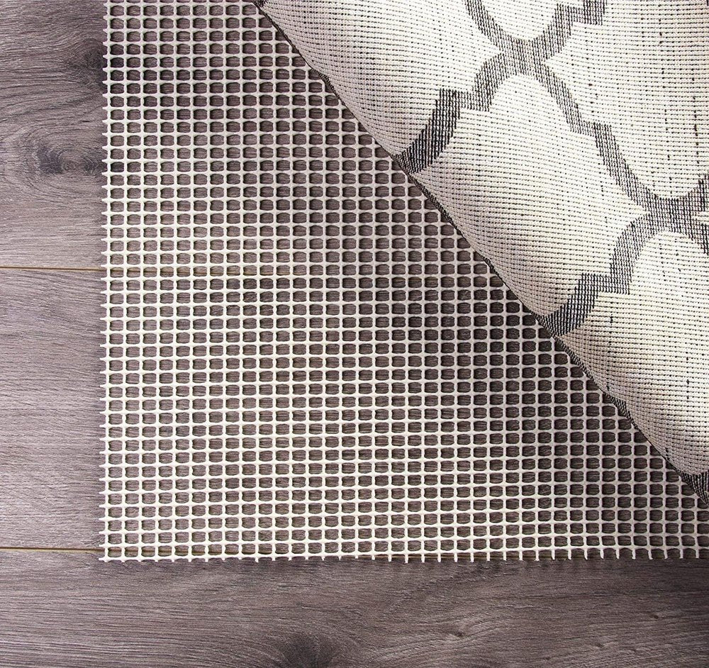 6' x 9' Ivory Striped Weave Non Slip Rug Pad styled in a furnished interior with a gray wall on a tiled floor.