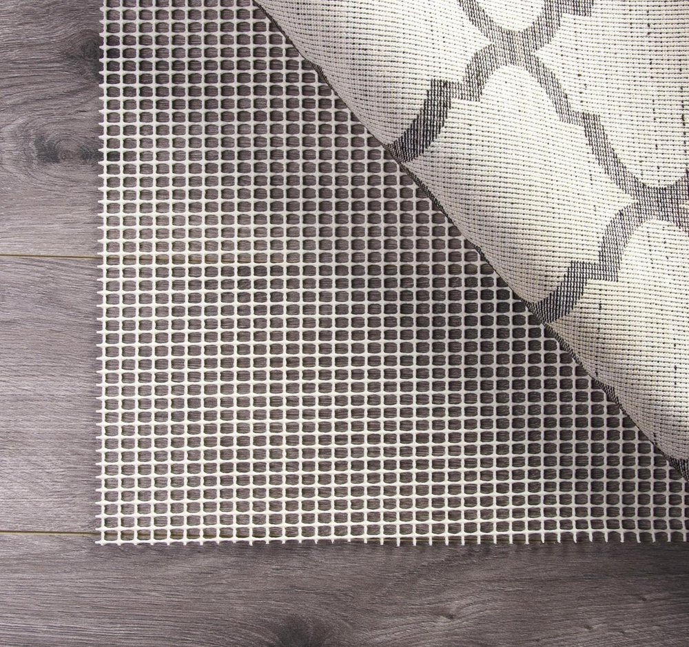 6' x 9' Ivory Striped Weave Non Slip Rug Pad styled in a furnished interior with a gray wall on a tiled floor.