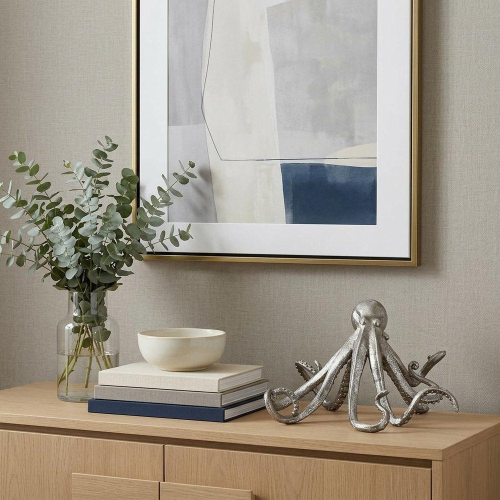 12" Antiqued Silver Resin Octopus Tabletop Sculpture styled in a furnished interior with a light gray wall on a wood floor.