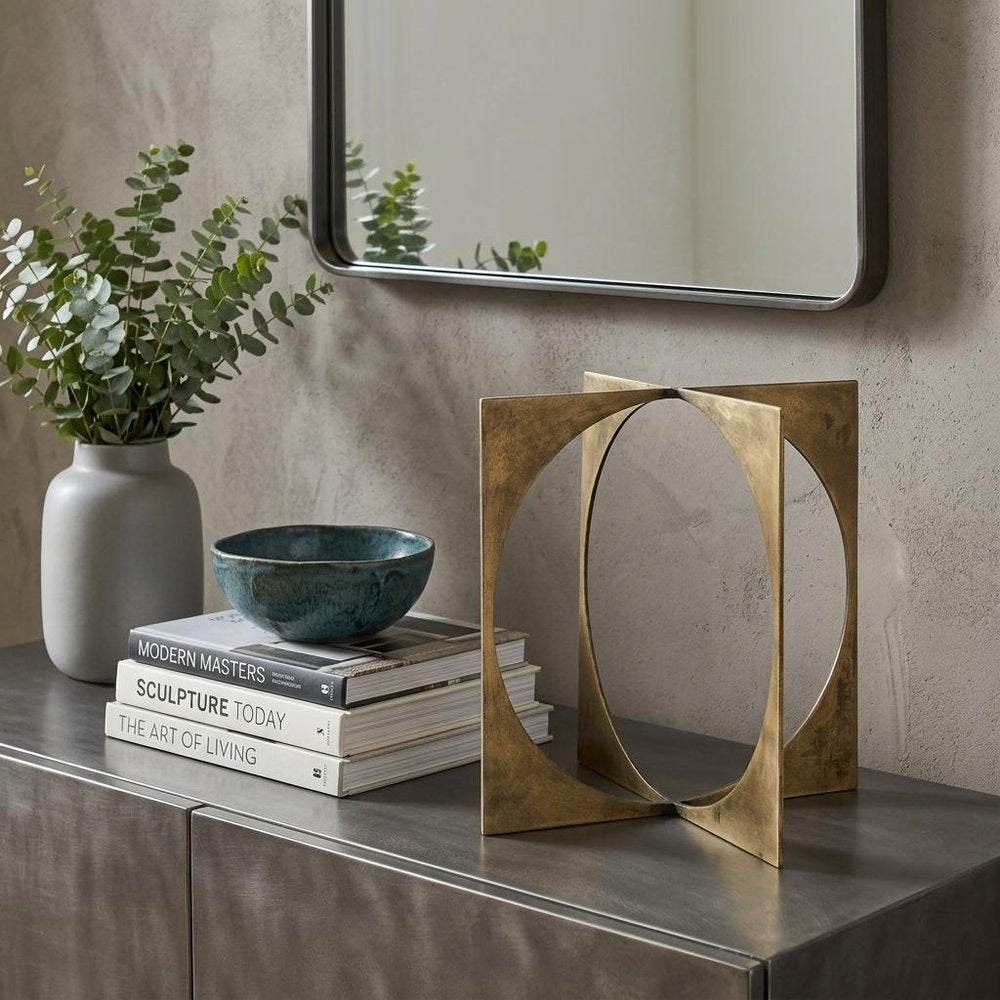 10" Burnished Gold Metal Circle Square Sculpture styled in a furnished interior with a light gray wall on a dark wood floor.