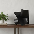 12" Contempo Antiqued Black Abstract Sculpture styled in a furnished interior with an off-white wall on a tiled floor.