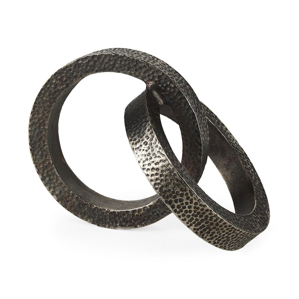 Gray hammered metal sculpture of two interlocking rings on a white background.