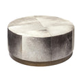 Round ottoman with patchwork gray and white cowhide upholstery and a brass base on a white background.