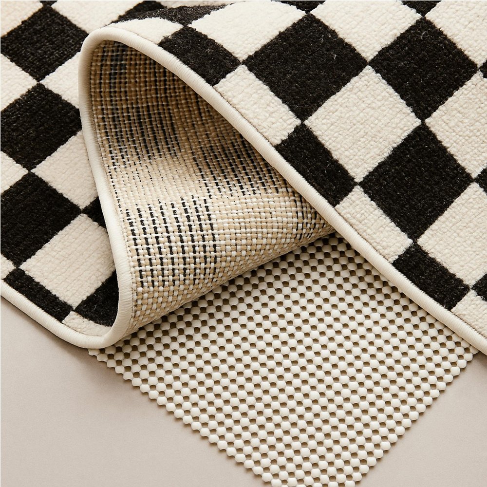 6' x 9' Ivory Striped Weave Non Slip Rug Pad styled in a furnished interior with a black wall on a tiled floor.