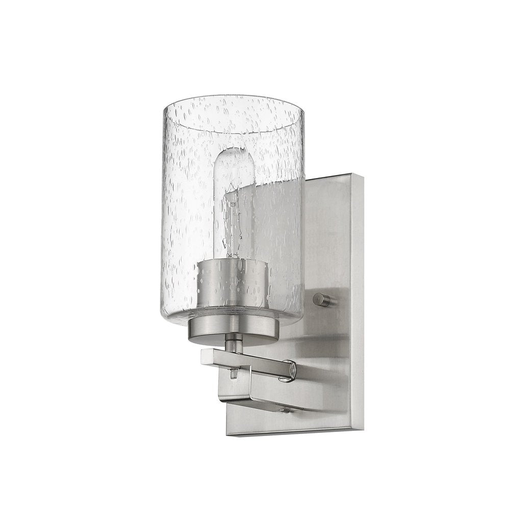 Silver metal wall sconce with a clear textured glass shade and exposed bulb on a white background.