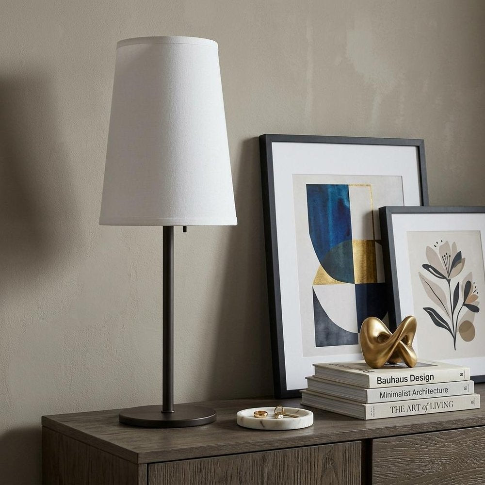 27" Black Metal Table Lamp With White Cone Shade displayed on a dark wood tabletop in a furnished interior against a tan wall.