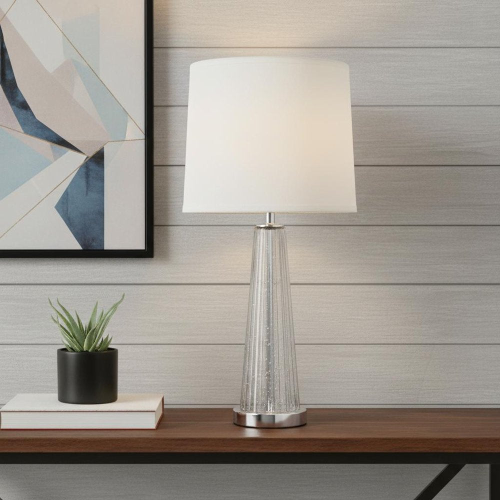 29" Clear And Silver Table Lamp With Empire Shade displayed on a tabletop in a furnished interior against a light gray wall.