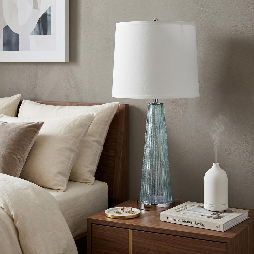 29" Aqua Glass Buffet Lamp With Off White Empire Shade styled in a furnished interior with a light gray wall on a dark wood floor in off-white glass.