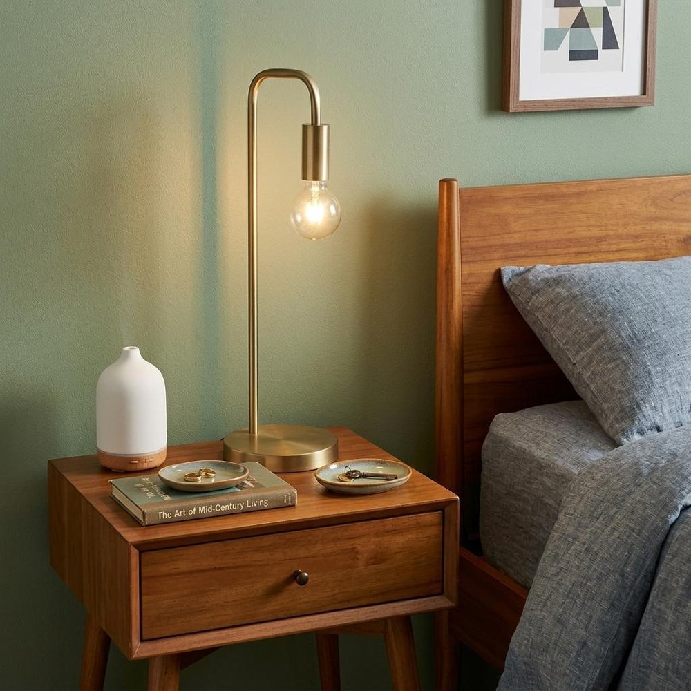 26" Brass Metal Table Lamp displayed on a tabletop in a furnished interior against a gold wall.