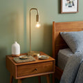 26" Brass Metal Table Lamp displayed on a tabletop in a furnished interior against a gold wall.