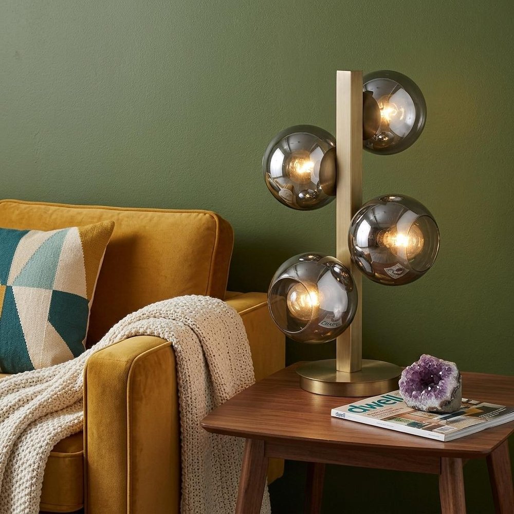 24" Brass Metal Four Light Novelty Table Lamp With Silver Metallic Globe Shades displayed on a dark wood tabletop in a furnished interior against a olive wall.