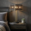25" Brass Metal Four Light Geometric Table Lamp With Black Drum Shade displayed on a tabletop in a furnished interior against a dark wall.