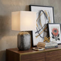 25" Blue and Gray Ceramic Table Lamp With White Square Shade displayed on a dark wood tabletop in a furnished interior against a tan wall.