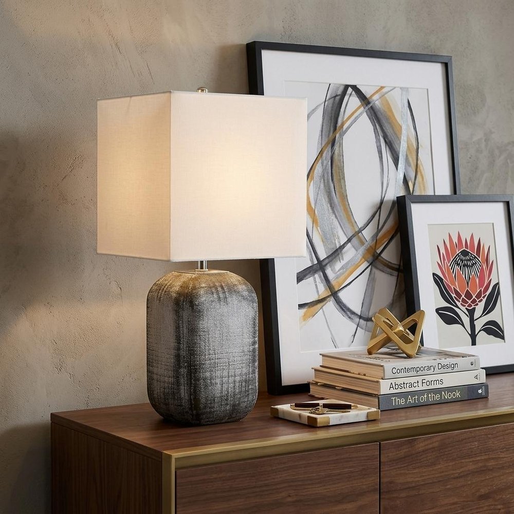 25" Blue and Gray Ceramic Table Lamp With White Square Shade displayed on a dark wood tabletop in a furnished interior against a tan wall.