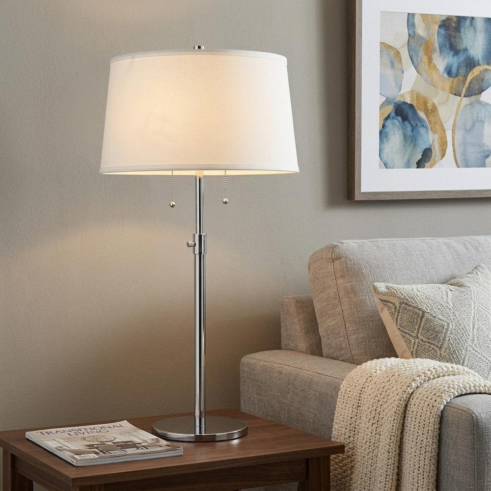 31" Silver Metal Two Light Adjustable Table Lamp With White Empire Shade displayed on a dark wood tabletop in a furnished interior against a tan wall.