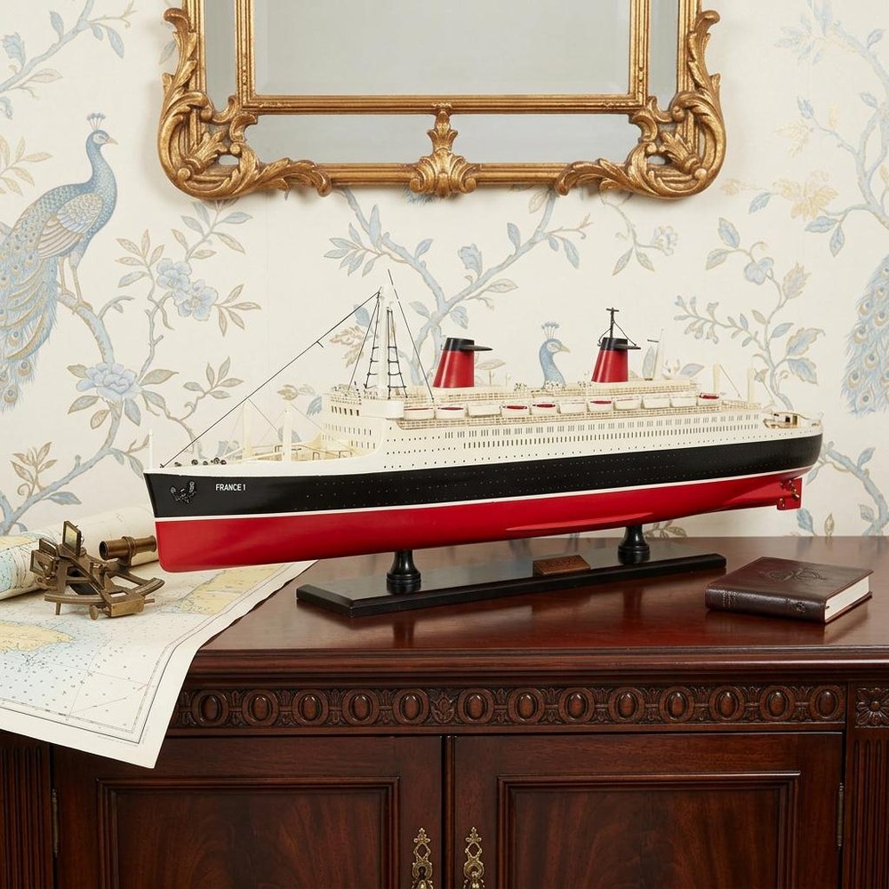 11" Black and Red SS France Boat Hand Painted Decorative Boat styled in a furnished interior with an off-white wall on a black floor.