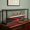15" Black and Red Solid Wood Hand Painted Normandie Large Display Case Model Boat styled in a furnished interior with a light gray wall on a black floor.
