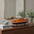 11" Maroon Staten Island Ferry Boat Hand Painted Decorative Boat styled in a furnished interior with a tan wall on a dark wood floor in dark brown.