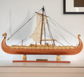 13" Wood Brown Solid Wood Hand Painted Model Boat Tabletop Sculpture styled in a furnished interior with an off-white wall on a wood floor.