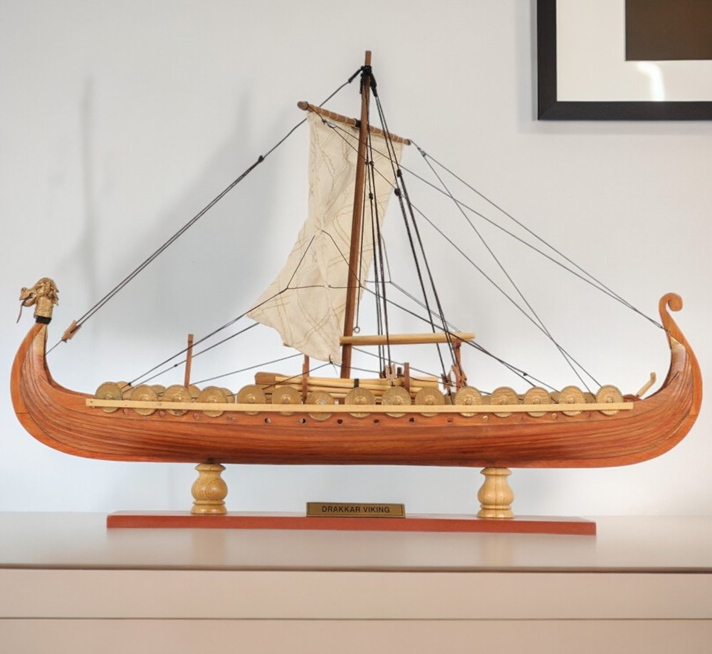 13" Wood Brown Solid Wood Hand Painted Model Boat Tabletop Sculpture styled in a furnished interior with an off-white wall on a wood floor.