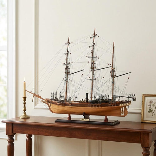 Wooden model of the CSS Alabama ship, with intricate rigging and sails, displayed on a dark stand on a wooden table.