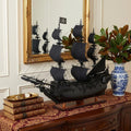 24" Black Solid Wood Hand Painted Model Boat Tabletop Sculpture styled in a furnished interior with a cream wall on a dark wood floor.