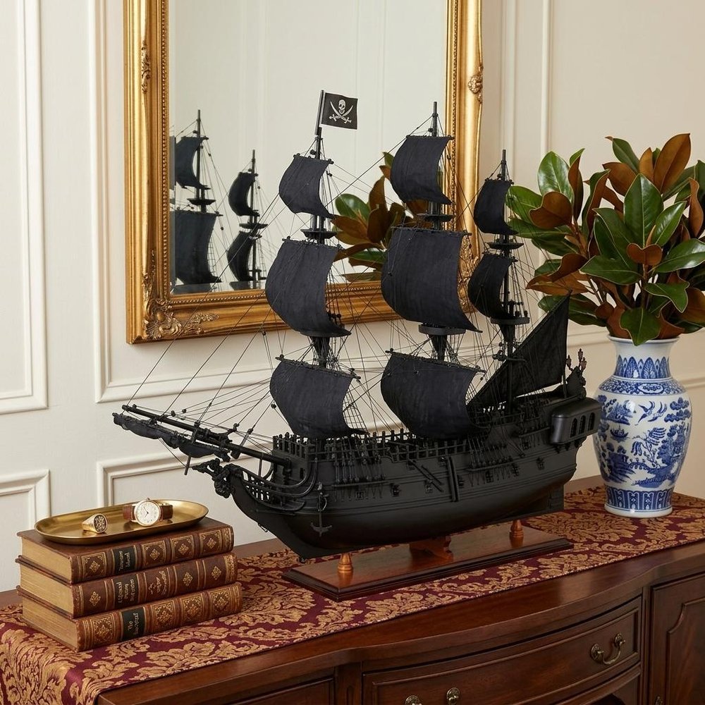 24" Black Solid Wood Hand Painted Model Boat Tabletop Sculpture styled in a furnished interior with a cream wall on a dark wood floor.