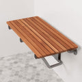 Wall-mounted teak shower bench with a natural wood finish on a white tiled wall and hexagonal floor.