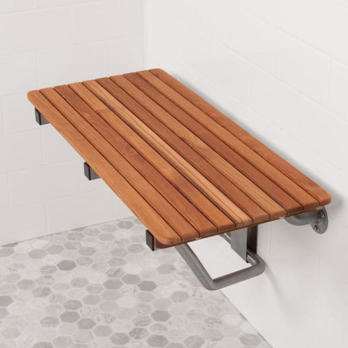Wall-mounted teak shower bench with a natural wood finish on a white tiled wall and hexagonal floor.