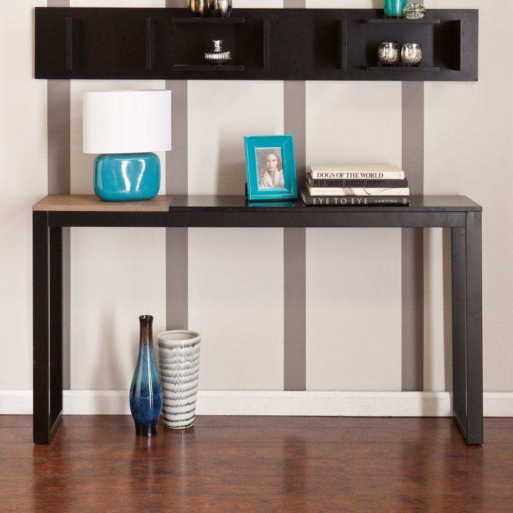 Black and natural wood sled console table with a lamp, photo frame, and books on top, against a striped wall.