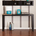 Black and natural wood sled console table with a lamp, photo frame, and books on top, against a striped wall.