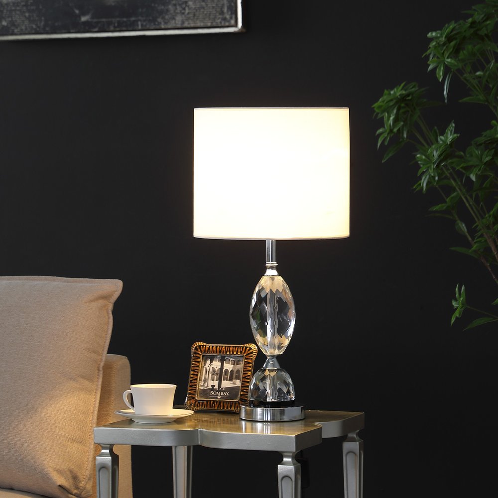 24" Silver Crystal Standard Table Lamp With White Shade displayed on a tabletop in a furnished interior against a black wall.