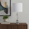 24" Silver Crystal Standard Table Lamp With White Shade displayed on a dark wood tabletop in a furnished interior against a light gray wall.