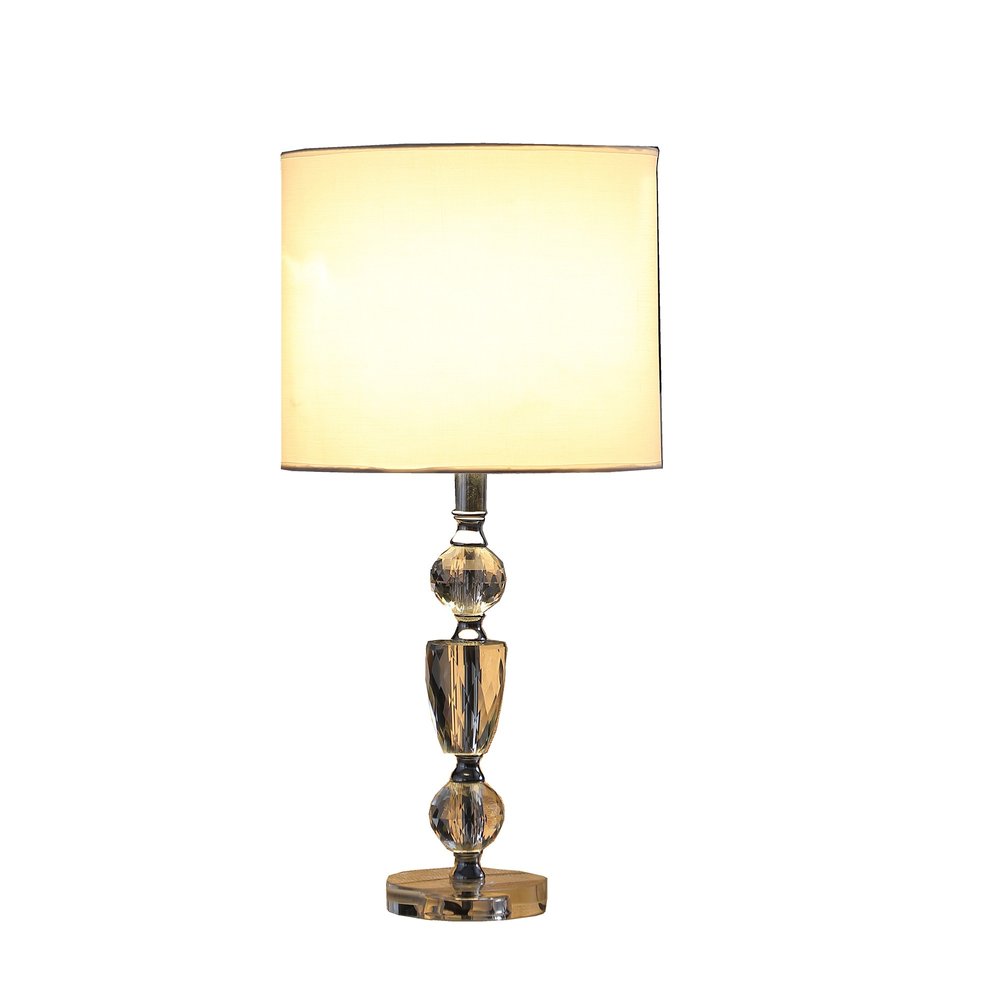 24" Clear And Silver Faux Crystal And Metal Table Lamp With White Drum Shade. Table lamp isolated on a plain white background, in a white crystal finish.