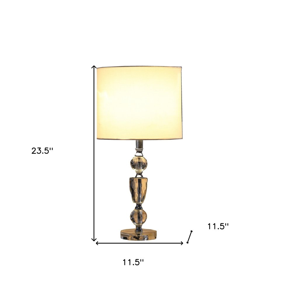 24" Clear And Silver Faux Crystal And Metal Table Lamp With White Drum Shade. Table lamp isolated on a plain white background, finished in white crystal.