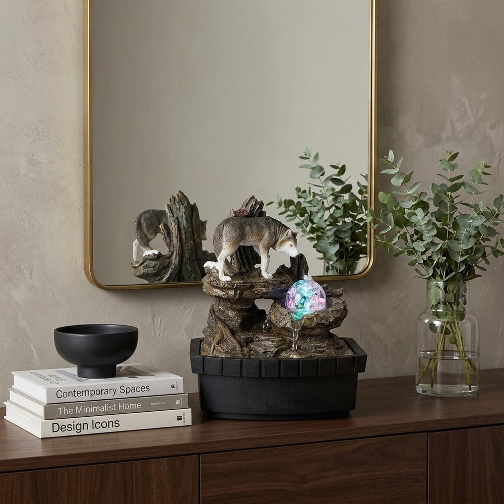 10" Black Polyresin Wolf Tabletop Fountain Sculpture styled in a furnished interior with a tan wall on a dark wood floor.