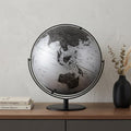 21" Black And Silver Modern Polyresin Globe styled in a furnished interior with a light gray wall on a charcoal floor.