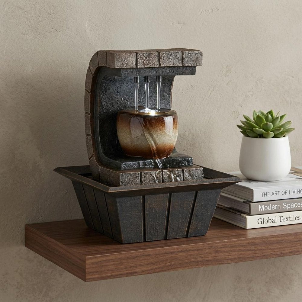 10" Brown Textured Polyresin Tabletop Fountain with LED Light styled in a furnished interior with a cream wall on a wood floor.