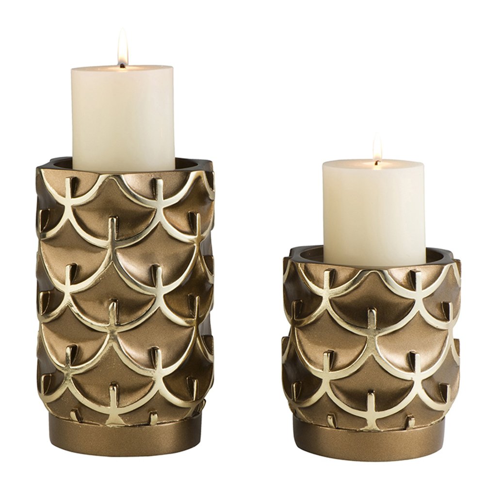 Two antiqued brass pillar candle holders with a raised scale pattern on a white background.