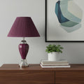 27" Silver Ceramic Bedside Table Lamp With Magenta Empire Shade displayed on a dark wood tabletop in a furnished interior against a light gray wall.