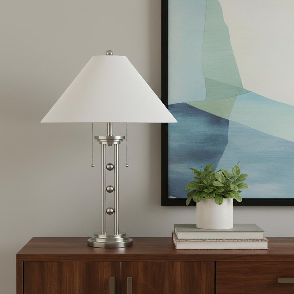 27" Silver Metal Two Light Table Lamp With White Classic Empire Shade displayed on a dark wood tabletop in a furnished interior against a light gray wall.