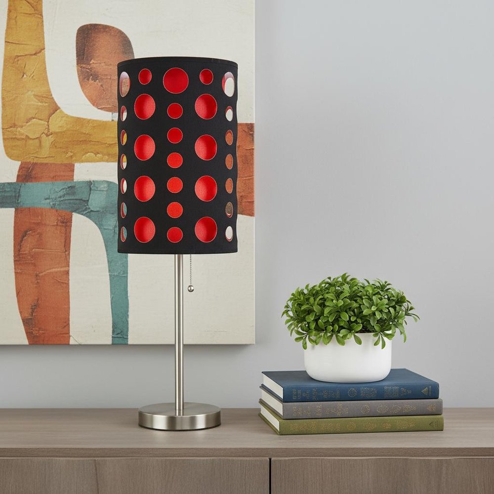 33" Steel Mod Table Lamp With Black And Red Drum Shade displayed on a dark wood tabletop in a furnished interior against a light gray wall.