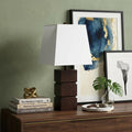 27" Brown Bedside Table Lamp With White Shade displayed on a dark wood tabletop in a furnished interior against a gold wall.