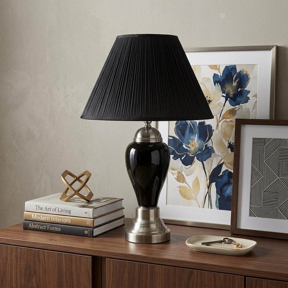 27" Black and Silver Ceramic Urn Table Lamp With Black Empire Shade displayed on a dark wood tabletop in a furnished interior against a light gray wall.