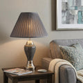 27" Gray and Silver Metal Urn Table Lamp With Gray Empire Shade displayed on a dark wood tabletop in a furnished interior against a tan wall.