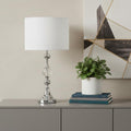 30" Silver Metal Bedside Table Lamp With White Classic Drum Shade displayed on a tabletop in a furnished interior against a cream wall.