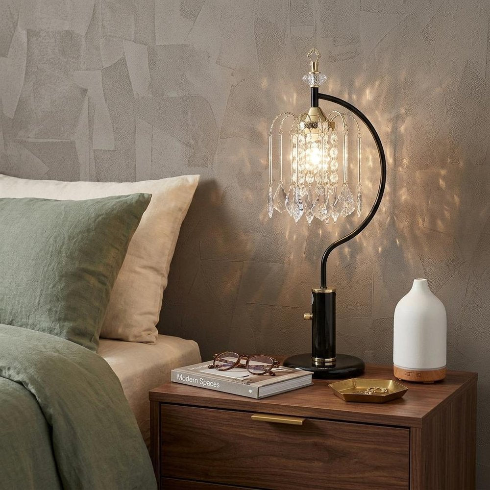 27" Black and Gold Metal Faux Crystal Chandelier Table Lamp displayed on a dark wood tabletop in a furnished interior against a tan wall.