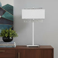 28" Silver Table Lamp With Faux Crystals and White Rectangle Shade displayed on a dark wood tabletop in a furnished interior against a light gray wall.