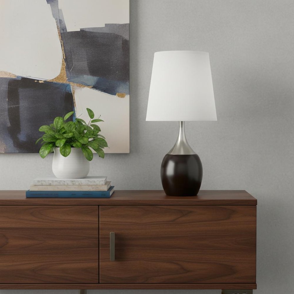 25" Black and Silver Gourd Table Lamp With White Tapered Drum Shade displayed on a dark wood tabletop in a furnished interior against a light gray wall.