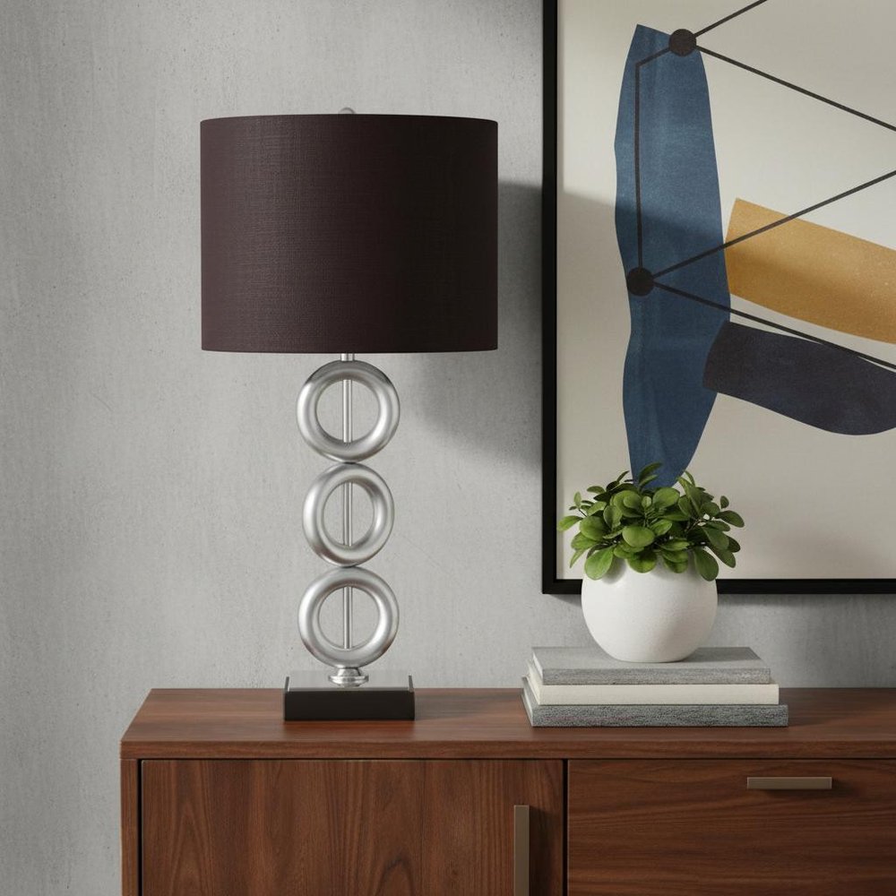 29" Silver Ceramic Geometric Table Lamp With Brown Classic Drum Shade displayed on a dark wood tabletop in a furnished interior against a light gray wall.